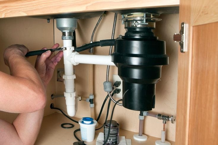 Plumber installing a garbage disposal beneath a kitchen sink in Clearwater